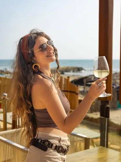 A lifestyle shot of a woman enjoying a glass of white wine by the sea, selling a relaxed and luxurious experience.