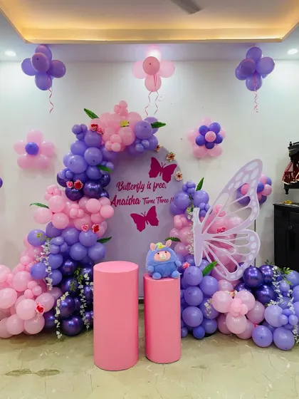 A full view of a beautiful butterfly-themed third birthday. The setup includes a custom backdrop, a pink and purple balloon arch, and butterfly wing props.
