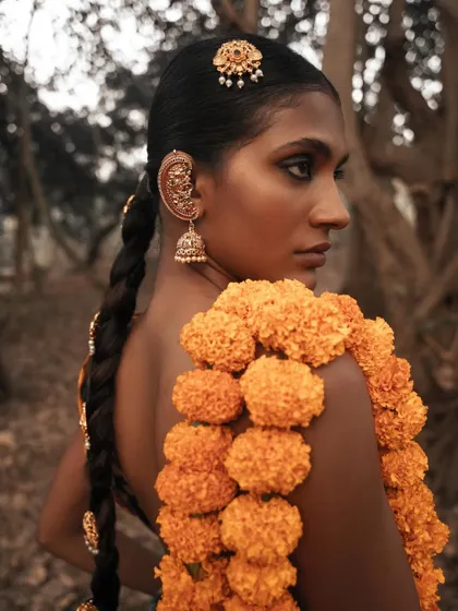 A profile shot focusing on the traditional jewelry and the contrast between the bright flowers and the earthy tones of the forest.