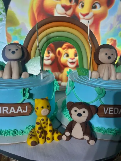 A closer look at the twin animal themed cakes, showing the personalized names and handcrafted fondant giraffe and monkey.