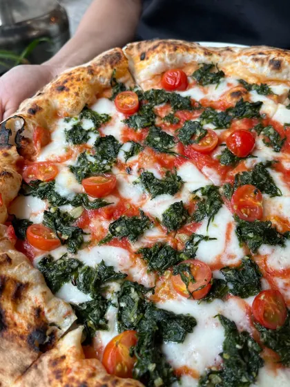 A close-up of the Spinach and Garlic pizza, showing the fresh cherry tomatoes and wilted spinach.