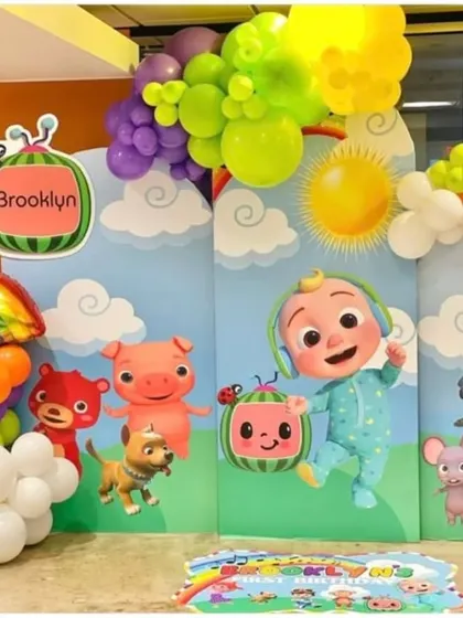 A bright and cheerful Cocomelon theme party. This setup includes a large backdrop with all the favorite characters, a rainbow balloon garland, and personalized floor signage.