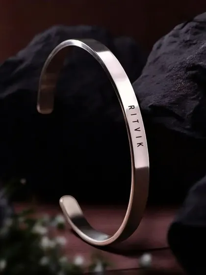 A silver-finish cuff bracelet engraved with 'RITVIK', displayed against a dark, textured rock. This highlights the contrast and clean lines of the engraving.