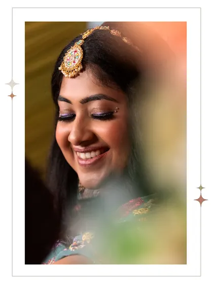 A close-up of the bride's joyful smile during her Mehendi. The soft, colorful blur in the foreground adds an artistic touch, focusing all the attention on her radiant expression.