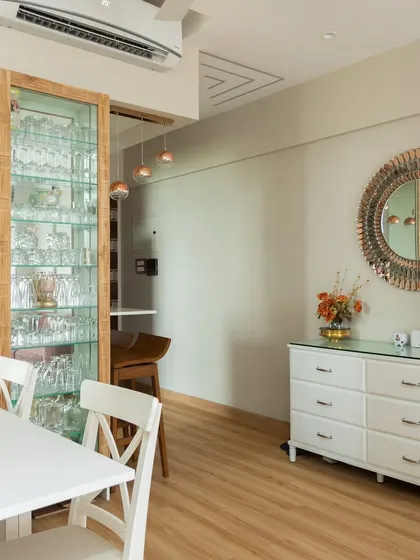 This dining area features a beautiful glass-front crockery unit with internal lighting, a classic white dining set, and a statement mirror to make the space feel larger.