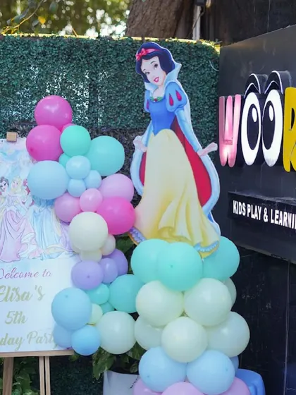 A Snow White themed entrance decoration, featuring a character cutout and a colorful balloon garland.