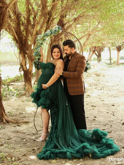 A quiet, romantic moment during an outdoor maternity shoot. The couple is framed by trees and a beautiful birdcage prop, adding a touch of whimsy to their portrait.