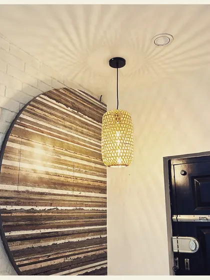 This cylindrical woven pendant light casts a stunning starburst pattern on the ceiling. We paired it with a large, circular wooden wall art piece to create a composition of natural textures and warm, ambient light.
