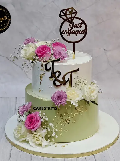 A beautiful two-tier engagement cake combining Black Forest and Butterscotch flavors. This 5kg creation is decorated with fresh pink and white carnations, gold leaf, and a custom initial topper.