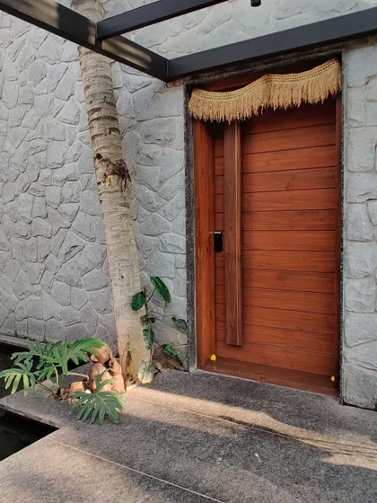 Sunlight filters through the canopy, highlighting the textures of the stone wall and wooden door at the entrance.