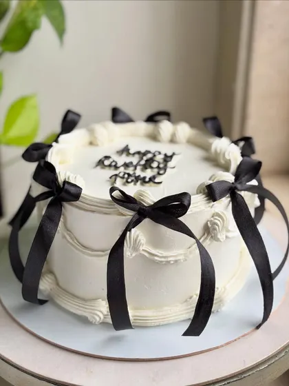 The full view of the balletcore-inspired cake, showing how the black ribbons create a dramatic and chic contrast against the soft white buttercream.