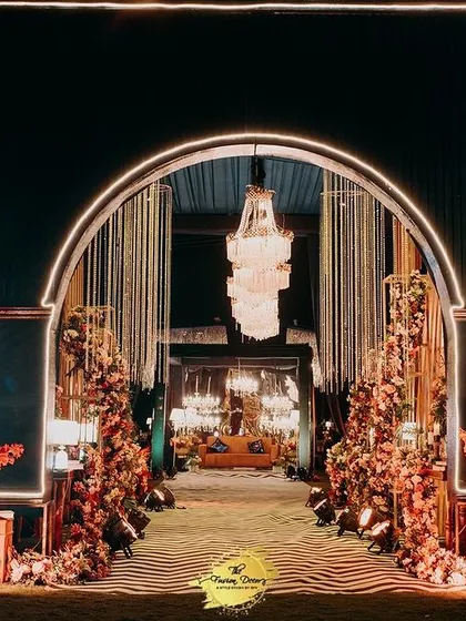 A radiant entrance for a night of glamour. This arched gateway, illuminated with warm lights and flanked by intricate decor panels, sets a sophisticated tone for an unforgettable cocktail or sangeet evening.