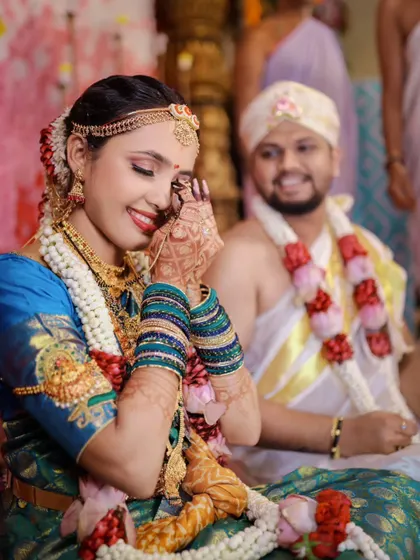 A shy, happy smile from the bride during her wedding ceremony, with the groom looking on fondly in the background.