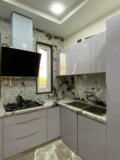A beautiful L-shaped kitchen with light purple handleless cabinets and a striking granite countertop and backsplash. The design makes excellent use of a compact space with a window.