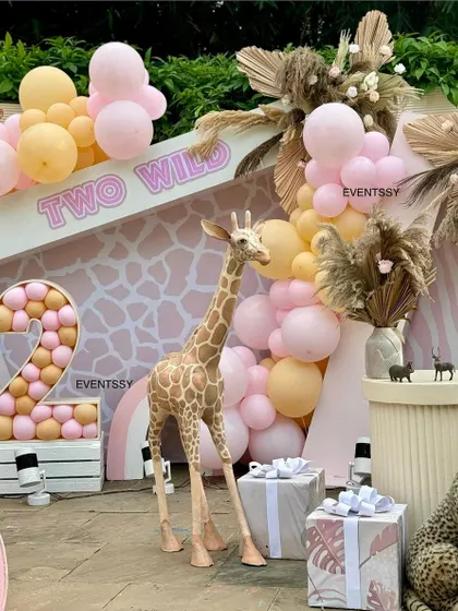 A detail shot from the "Two Wild" party, focusing on the giraffe prop and the balloon-filled marquee number "2." The giraffe-print backdrop adds another layer of texture to the design.
