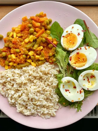 This balanced plate features brown rice, mixed vegetable curry, boiled eggs, and a side of fresh greens.