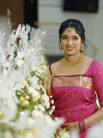The bride posing next to floral arrangements. The soft lighting highlights her glowing skin and elegant makeup.