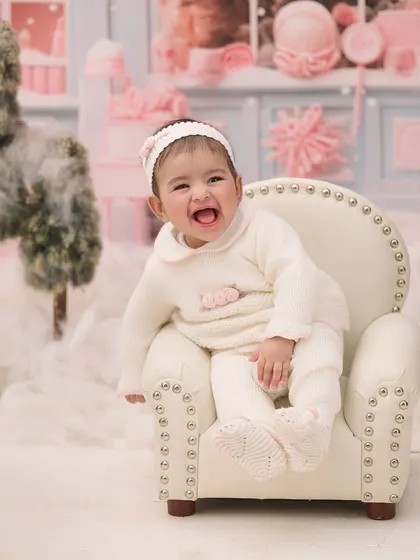 A cozy winter wonderland scene. This baby girl's joyful expression lights up the snowy, pink-themed set.