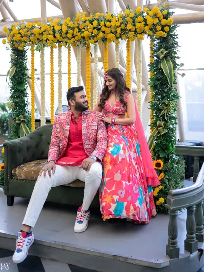 The couple relaxes on a sofa against a backdrop of vibrant yellow and green Haldi decor.