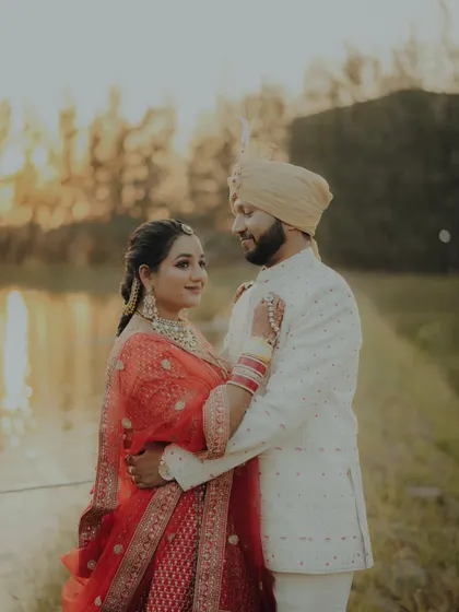 A beautiful pre-wedding portrait by the water. The couple shares a loving glance, their traditional outfits glowing in the warm sunset light.