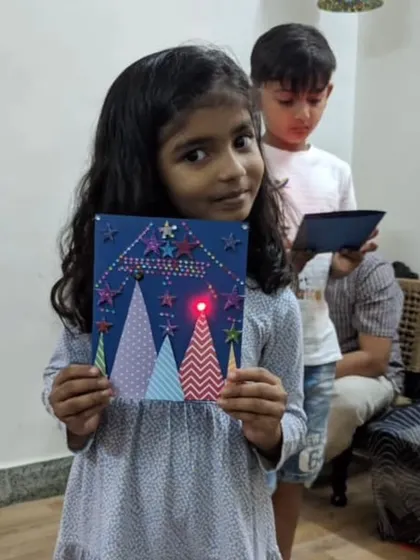For a Christmas-themed party, a girl shows her festive light-up greeting card, complete with a glowing red LED light.
