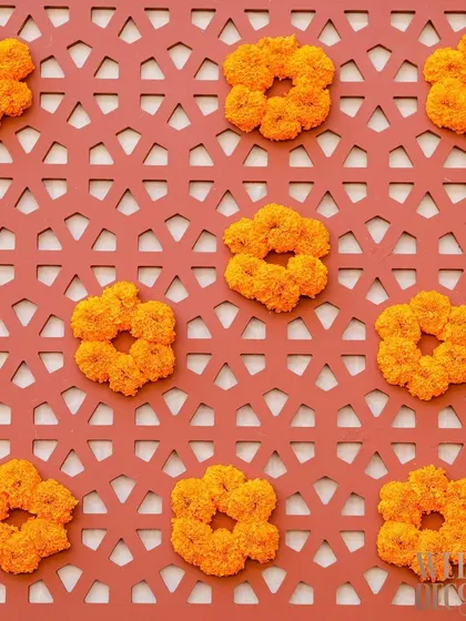 A close-up of a custom jali panel in a terracotta hue, decorated with small, circular marigold arrangements. This detail adds texture and a traditional touch to the decor.