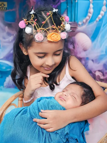 A close-up showing the gentle and loving gaze of a big sister looking at her sleeping newborn brother.