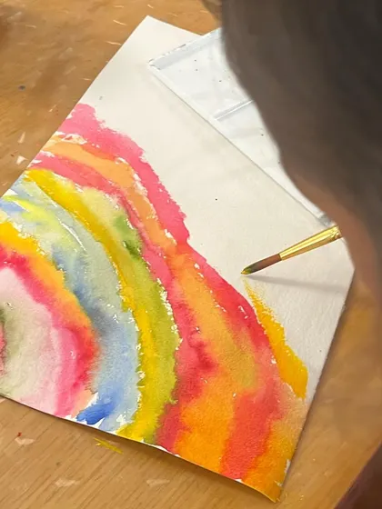 A young artist paints beautiful, flowing rainbow waves. We encourage children to move beyond rigid lines and explore organic shapes and patterns in their work.