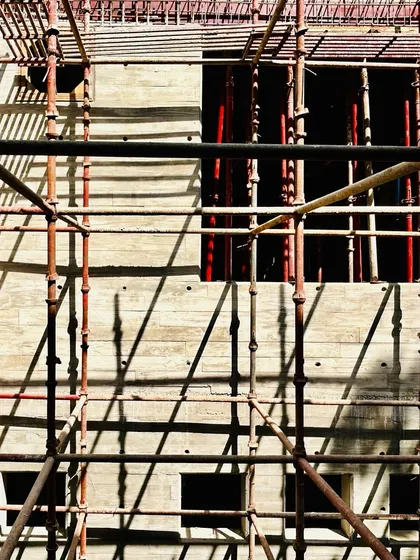 A detail of window openings being formed in a concrete wall at a residence in New Delhi. The scaffolding creates a grid-like pattern of light and shadow on the surface.