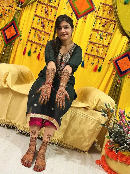 A lovely photo of a bride in her mehndi ceremony outfit, showing her beautiful hand and feet designs.
