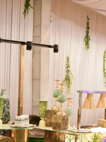 A modern and stylish buffet corner featuring geometric gold decor pieces, green vases, and elegant candle holders. This setup reflects a contemporary and chic event theme.