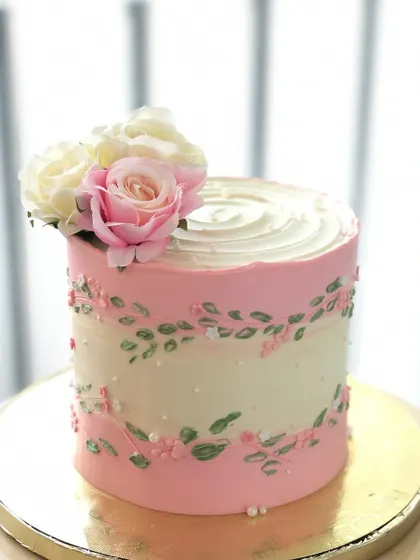 A simple and pretty cake with a pink and white design, delicate leaf piping, and a few fresh roses.