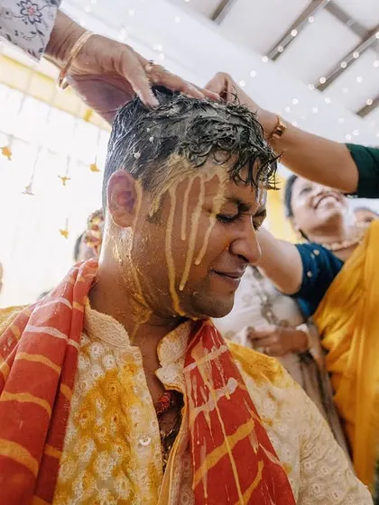 A candid moment of family members joyfully applying haldi to the groom. The little girl's expression in the background adds another layer to the story.