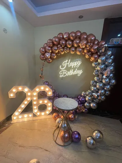 This is a duplicate of ID 37, 80, 136, 139, 151, 203, 247. A stylish half-arch balloon ring for a 26th birthday. This home decoration uses chrome rose gold and silver balloons, a neon sign, and marquee numbers.