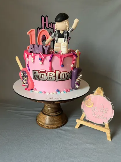 A fun and vibrant Roblox-themed cake for a 10th birthday. It includes a custom fondant character, the game's logo, and a pink drip effect.