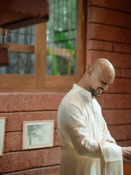 A candid portrait of the groom getting ready, capturing a quiet, natural moment of adjustment to his traditional attire before the shoot.