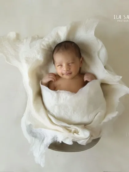 A beautiful, minimalist newborn portrait. The baby is wrapped snugly in a textured white fabric, creating a look that is both artistic and timeless.