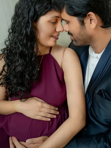 A close-up, intimate shot capturing the tender connection between the expecting couple. The focus is on their expressions and the gentle way they hold the baby bump.