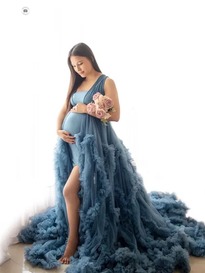 A full-length solo portrait against a bright white background, highlighting the beautiful silhouette of the mother-to-be in her blue gown.