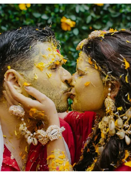 An intimate and playful kiss between the couple, their faces covered in turmeric and flower petals.