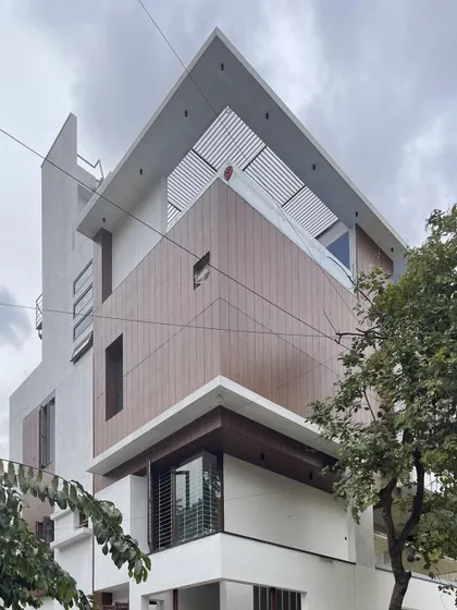The angular composition of this facade combines wood-look cladding and white planes, with a slatted pergola on the roof adding texture and filtering sunlight.