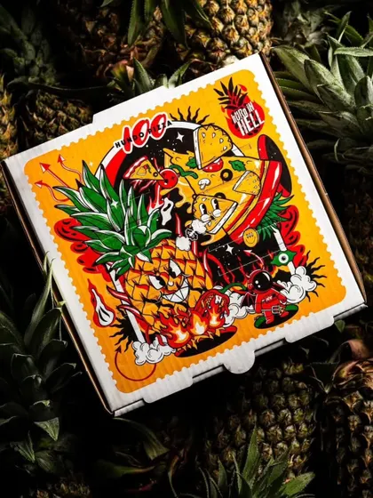 A top-down shot of the Hundo Pizza box, featuring its unique and artistic illustration, set against a bed of pineapples.