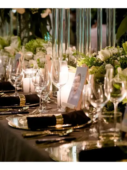 A close up of a sophisticated table setting for a formal birthday dinner. The combination of classic white and gold dinnerware, crystal glassware, and soft candlelight reflects our attention to detail in creating a refined ambiance.
