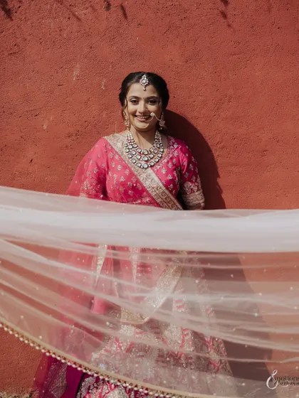 A playful and happy portrait of the bride Shreya, her veil flowing in the wind against a vibrant red wall.