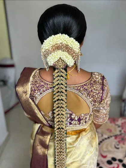 A back view of a stunning muhurtham hairstyle, featuring a full 'jada' made of gold accessories and fresh jasmine flowers, complementing the silk saree.