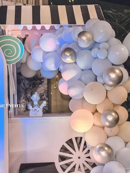 A detailed view of the candy cart at the pastel carnival, adorned with a beautiful balloon garland in shades of blue, white, and silver.