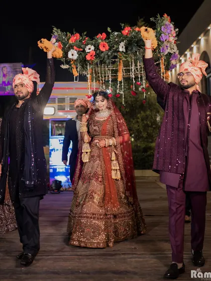 The bride's grand entrance under a 'phoolon ki chadar' (floral canopy) held by her brothers, a traditional and emotional moment.