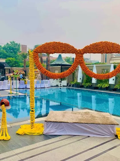 A fun and quirky poolside Haldi setup featuring a large pair of sunglasses made entirely of marigolds. This unique prop serves as a perfect photo opportunity for guests.