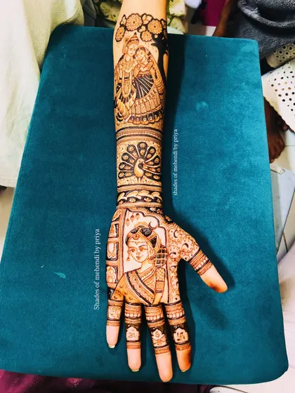 A full-arm bridal design combining multiple figures. The hand features a bride's portrait, while the arm depicts a Radha-Krishna scene, blending personal and devotional elements.