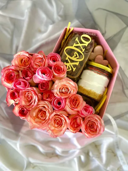 A heart-shaped gift box with an "XOXO" brownie slab, a jarred dessert, and a beautiful arrangement of fresh roses.